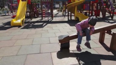 COVID 19 karantinası sırasında 6 yaşında bir kız salıncak dengeleyicisinde oturuyor ve ıskalıyor. Kamera, terk edilmiş bir oyun alanını göstererek soldan sağa dönüyor. Ukrayna; Kyiv; Tam HD, ses yok,