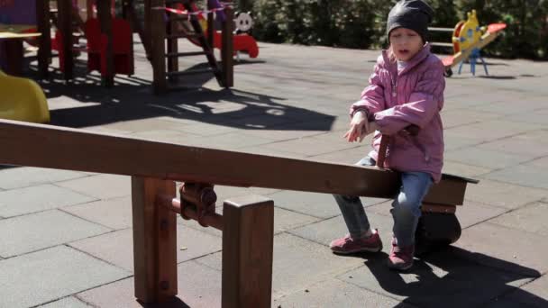 6歳の女の子は スイングバランサーに座っています 退屈と年 悲しいことにため息 立ち上がって 背景には人のいない遊び場があります 隔離中のウクライナキエフCovid フルHd — ストック動画