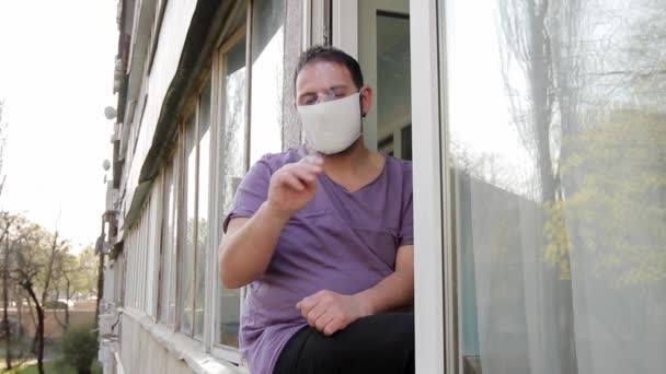 Een Man Met Een Medisch Masker Zit Een Raamkozijn Rookt — Stockvideo