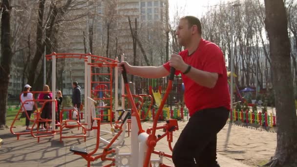 乌克兰 2020年4月5日在公共运动场上做运动的中年男子 下午在心血管设备上做运动 背景上有一群人在谈话 — 图库视频影像