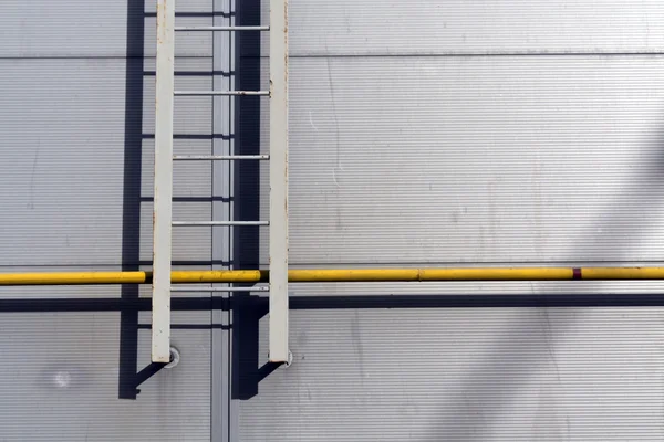 Ladder on grey wall and yellow tube. — Stock Photo, Image