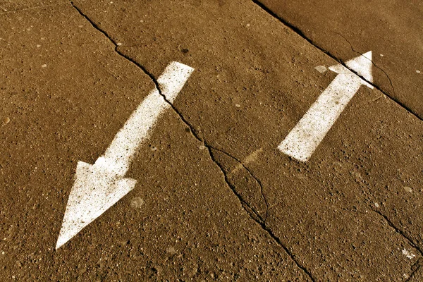 Two arrows on orange cracked asphalt surface.