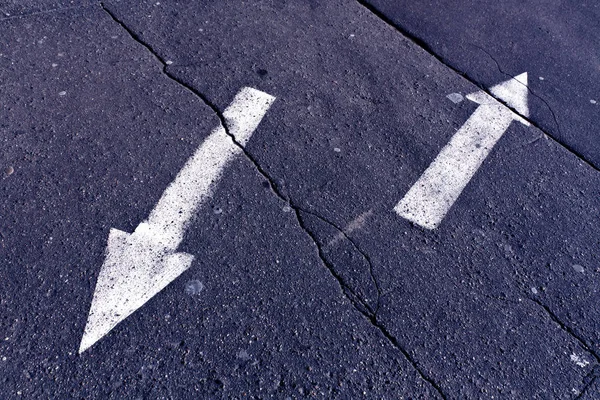 Two arrows on blue toned cracked asphalt surface.