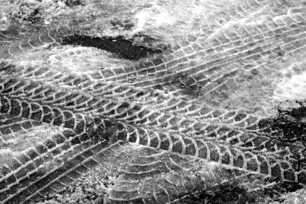 Tyre tracks on dirty snow in black and white.