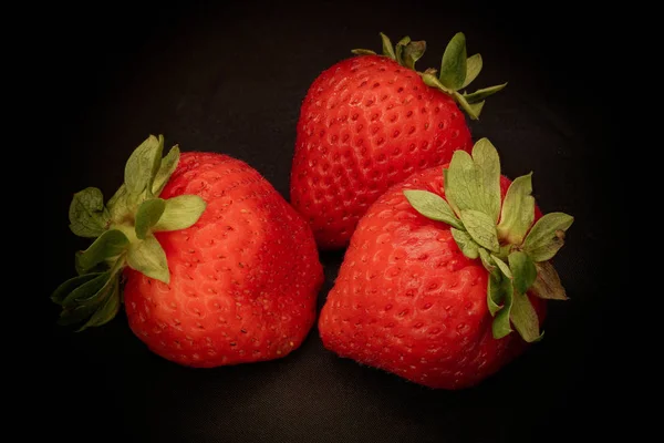Siyah bir zemin üzerine üç çilek Çilek