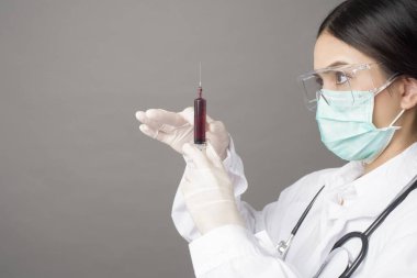 Cerrahi maskeli doktor kadın elinde şırınga tutuyor. 