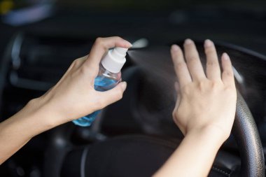 Kadın arabada ellerine dezenfektan püskürtüyor.