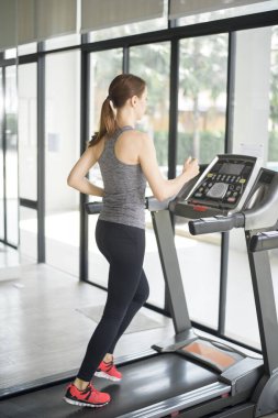 Spor salonundaki koşu bandında koşan genç ve güzel bir bayan sağlıklı bir hayat sürüyor. 