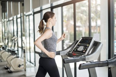 Spor salonundaki koşu bandında koşan genç ve güzel bir bayan sağlıklı bir hayat sürüyor. 