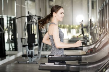 Spor salonundaki koşu bandında koşan genç ve güzel bir bayan sağlıklı bir hayat sürüyor. 