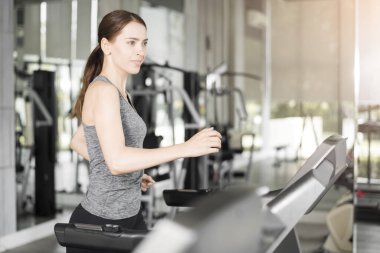 Spor salonundaki koşu bandında koşan genç ve güzel bir bayan sağlıklı bir hayat sürüyor. 