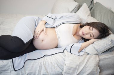 Güzel Asyalı hamile kadın yatakta uyuyor.