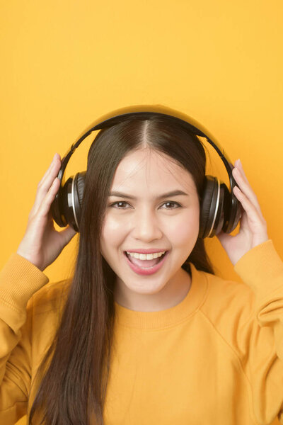 Music lover woman is enjoying with headset on yellow background 