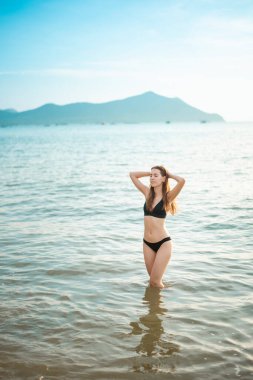 Siyah bikinili güzel kadın sahilde deniz suyuyla eğleniyor. 