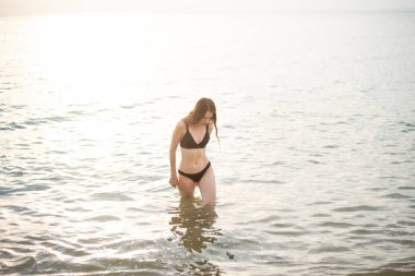 Siyah bikinili güzel kadın sahilde deniz suyuyla eğleniyor. 