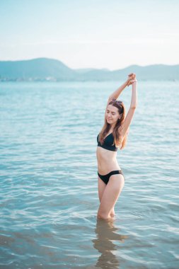 Siyah bikinili güzel kadın sahilde deniz suyuyla eğleniyor. 