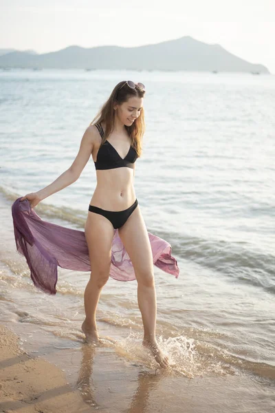 Beautiful woman in black bikini is walking on the beach