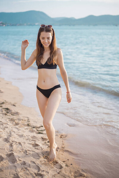 Beautiful woman in black bikini is walking from sea, summer concept 