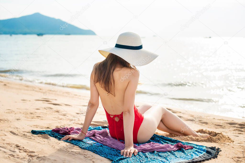 Back of Beautiful woman in red swimsuit is sitting on the beach 