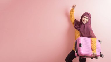 Başörtüsü olan Müslüman kadın pembe arka planda bavul tutuyor, insanlar seyahat konsepti. 