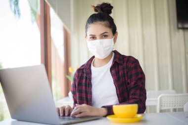 Maskeli güzel bir kadın kahve dükkanında bilgisayarla çalışıyor. 