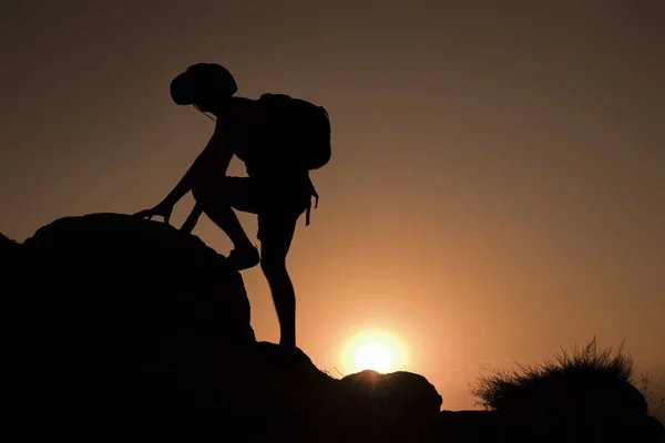 Silhouette of man climbing at sunset
