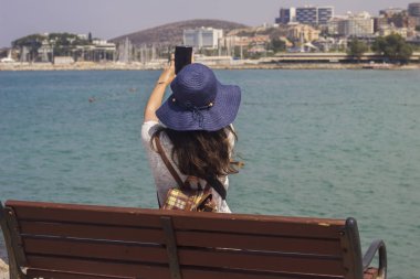 Deniz kenarındaki bir bankta oturan kadınlar, turistlerin özçekimlerini çekiyor.