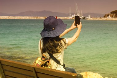 Deniz kenarındaki bir bankta oturan kadınlar, turistlerin özçekimlerini çekiyor.