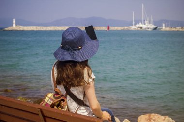 Deniz kenarındaki bir bankta oturan kadınlar, turistlerin özçekimlerini çekiyor.