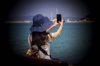 Deniz kenarındaki bir bankta oturan kadınlar, turistlerin özçekimlerini çekiyor.