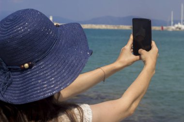 Deniz kenarındaki bir bankta oturan kadınlar, turistlerin özçekimlerini çekiyor.