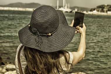 Deniz kenarındaki bir bankta oturan kadınlar, turistlerin özçekimlerini çekiyor.