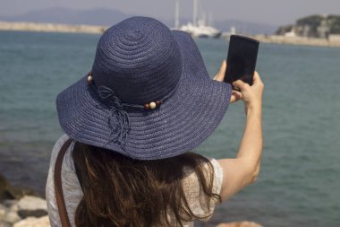 Deniz kenarındaki bir bankta oturan kadınlar, turistlerin özçekimlerini çekiyor.