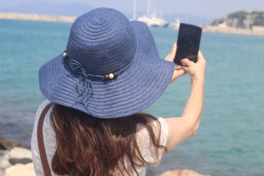 Deniz kenarındaki bir bankta oturan kadınlar, turistlerin özçekimlerini çekiyor.