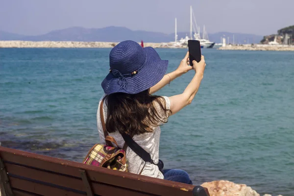 Deniz kenarındaki bir bankta oturan kadınlar, turistlerin özçekimlerini çekiyor.