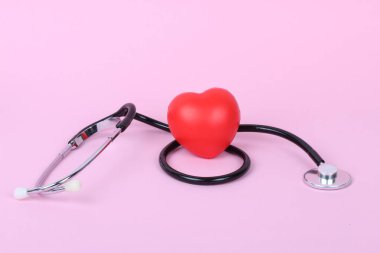 Stetoskop ve kalp pembe arka planda izole edilmiş.