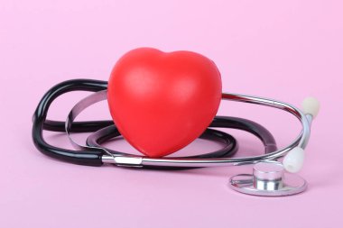 Stetoskop ve kalp pembe arka planda izole edilmiş.
