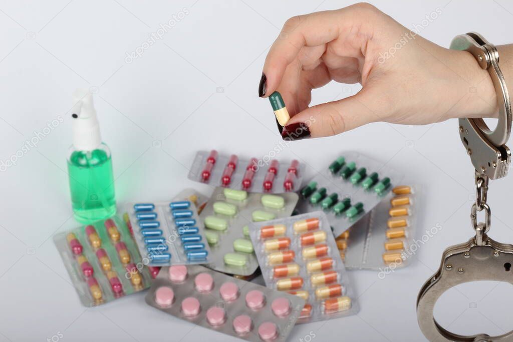 pills and tablets handcuffed hands on white background