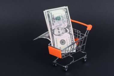İçinde dolar olan bir alışveriş arabası siyah üzerine izole edilmiş.