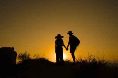 Sırt çantalı iki yürüyüşçünün siluetleri dağın tepesinden gün batımının keyfini çıkarıyorlar. Seyahat kavramı