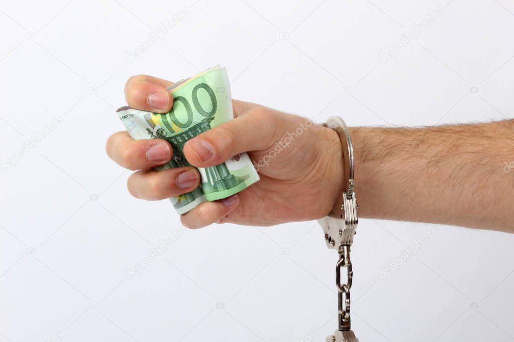 Male hand with handcuffs holding a lot of money