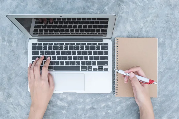 Primeros planos mujer tecleando a mano en el teclado en el ordenador portátil gris en el escritorio de hormigón fondo texturizado bajo la luz del día en el jardín en la vista superior, concepto de trabajo al aire libre — Foto de Stock