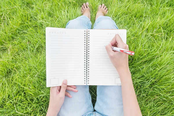 Primer plano asiático mujer sentado en hierba campo texturizado fondo para escribir en nota libro bajo luz del día en el jardín — Foto de Stock