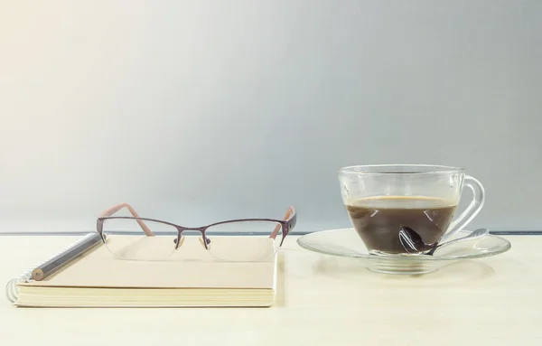 커피 브라운 노트 책의 투명 한 컵에 닫은 블랙 커피 흐리게 나무 책상에 안경과 직장 개념의 커피 휴식에 서리가 내린 유리 벽 질감 배경 — 스톡 사진