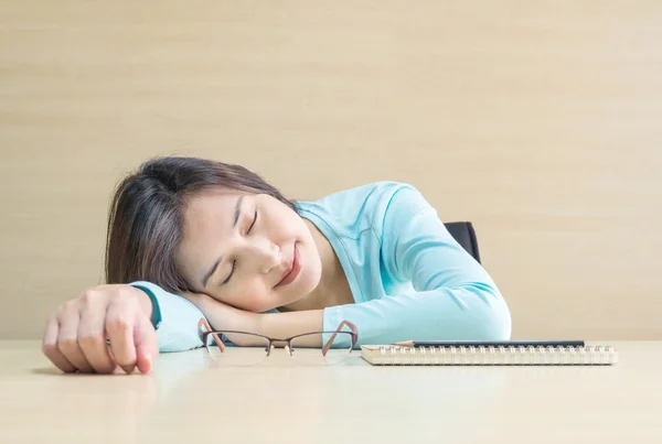 Asian woman sleep by lied on desk with happy face in rest time from reading book on blurred wooden desk and wall textured background in the meeting room , happy time and relaxation of woman concept