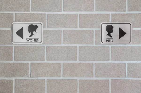 Zbliżenie aluminium znak WC dla kobiety i aluminium znak WC dla człowieka na ścianie cegły teksturowanej tła — Zdjęcie stockowe
