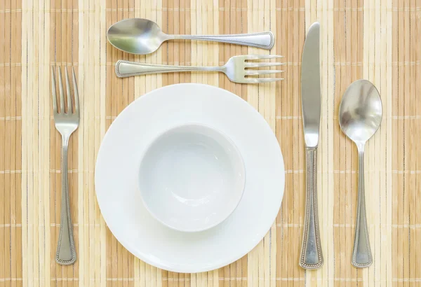 Plato y taza de cerámica blanca de primer plano con tenedor inoxidable y cuchara sobre alfombra de madera con textura de fondo en la mesa de comedor a la vista superior, grupo de vajilla antes de la cena — Foto de Stock