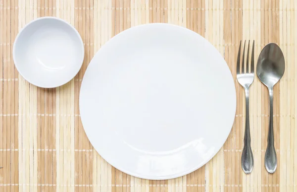 Plato y taza de cerámica blanca de primer plano con tenedor inoxidable y cuchara sobre alfombra de madera con textura de fondo en la mesa de comedor a la vista superior, grupo de vajilla antes de la cena — Foto de Stock