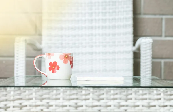 Nahaufnahme niedliche Tasse auf verschwommenem Holz weben Tisch und Stuhl strukturierten Hintergrund — Stockfoto