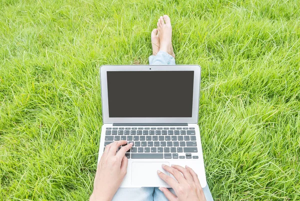 Mujer asiática sentada en el suelo de hierba en el fondo texturizado jardín para usar una computadora portátil, concepto de trabajo al aire libre — Foto de Stock